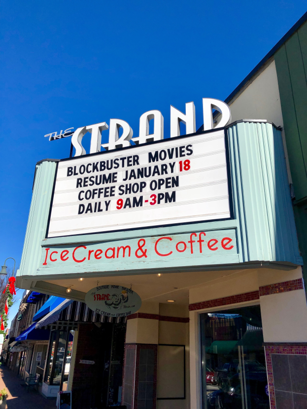 Der Strand-Blockbuster-Kino startet am 18. Januar Kaffee-Shop-Gebäude mit einem Namensschild, einem Straßenschild, einer Gruppe von Bäumen, einigen Topfpflanzen und einem bewölkten Himmel.