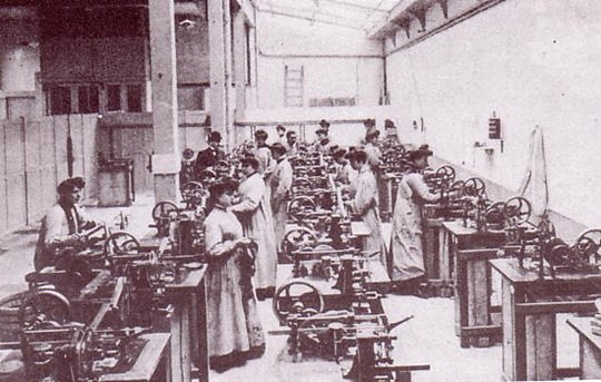 Schwarzes und weißes Bild von Menschen, die an Arbeitsplätzen in einer Fabrik arbeiten.